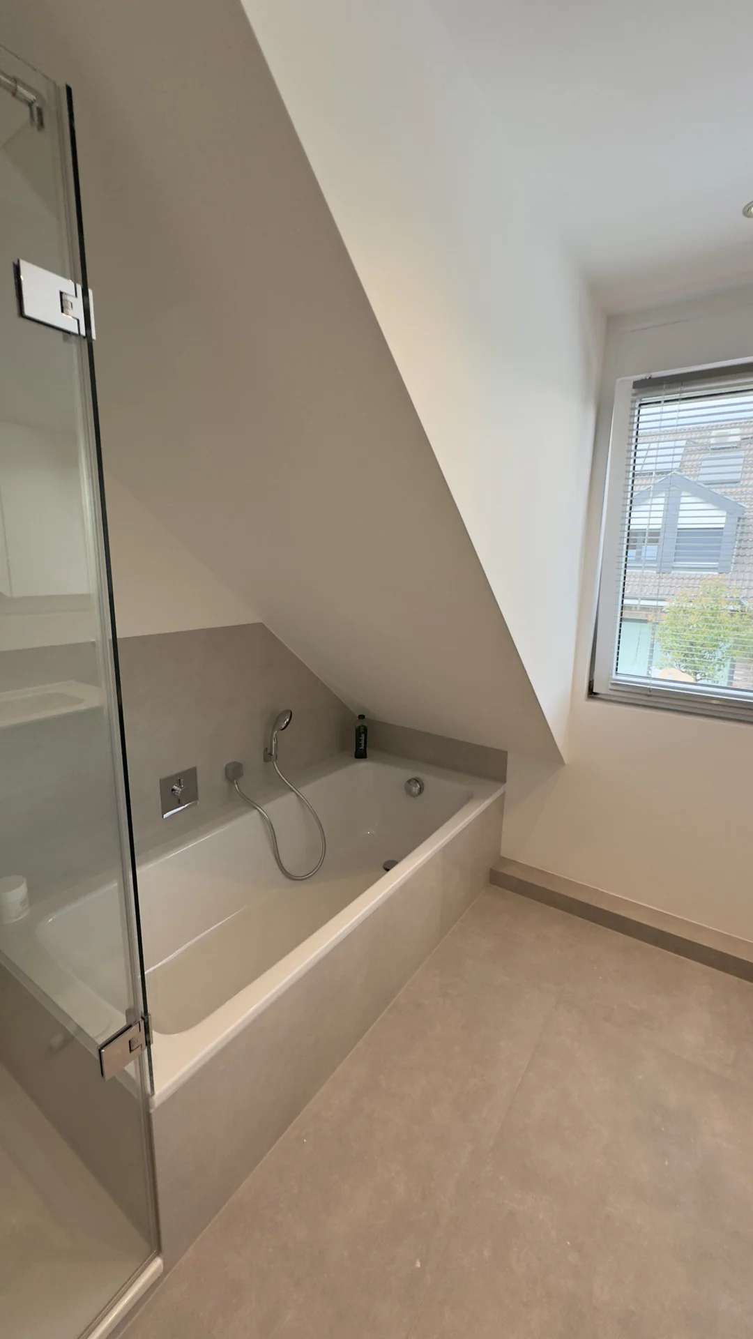 Eingeflieste Badewanne unter der Dachschräge neben einer Glasdusche